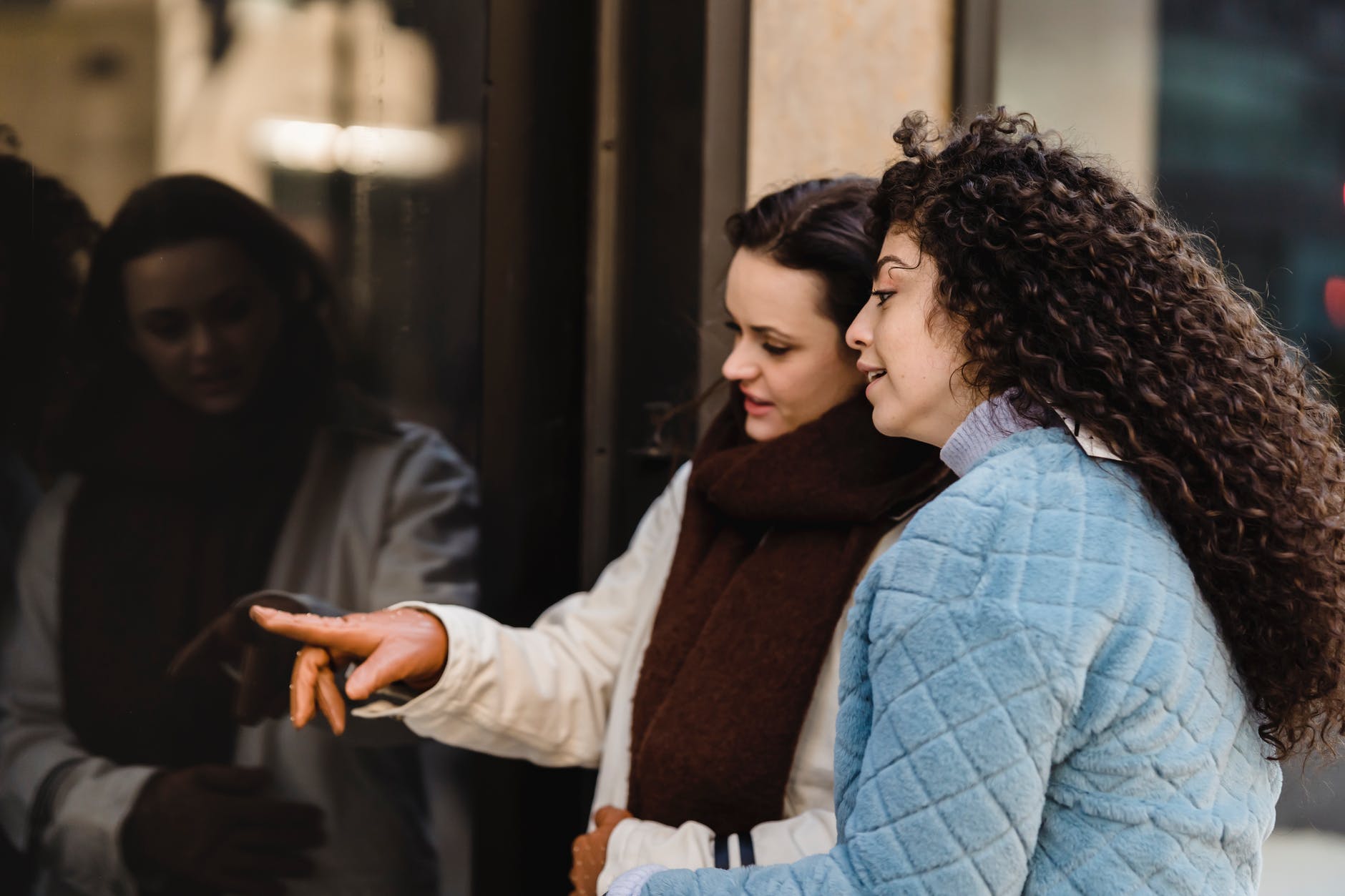 content young multiethnic women choosing clothes standing on street near boutique showcase